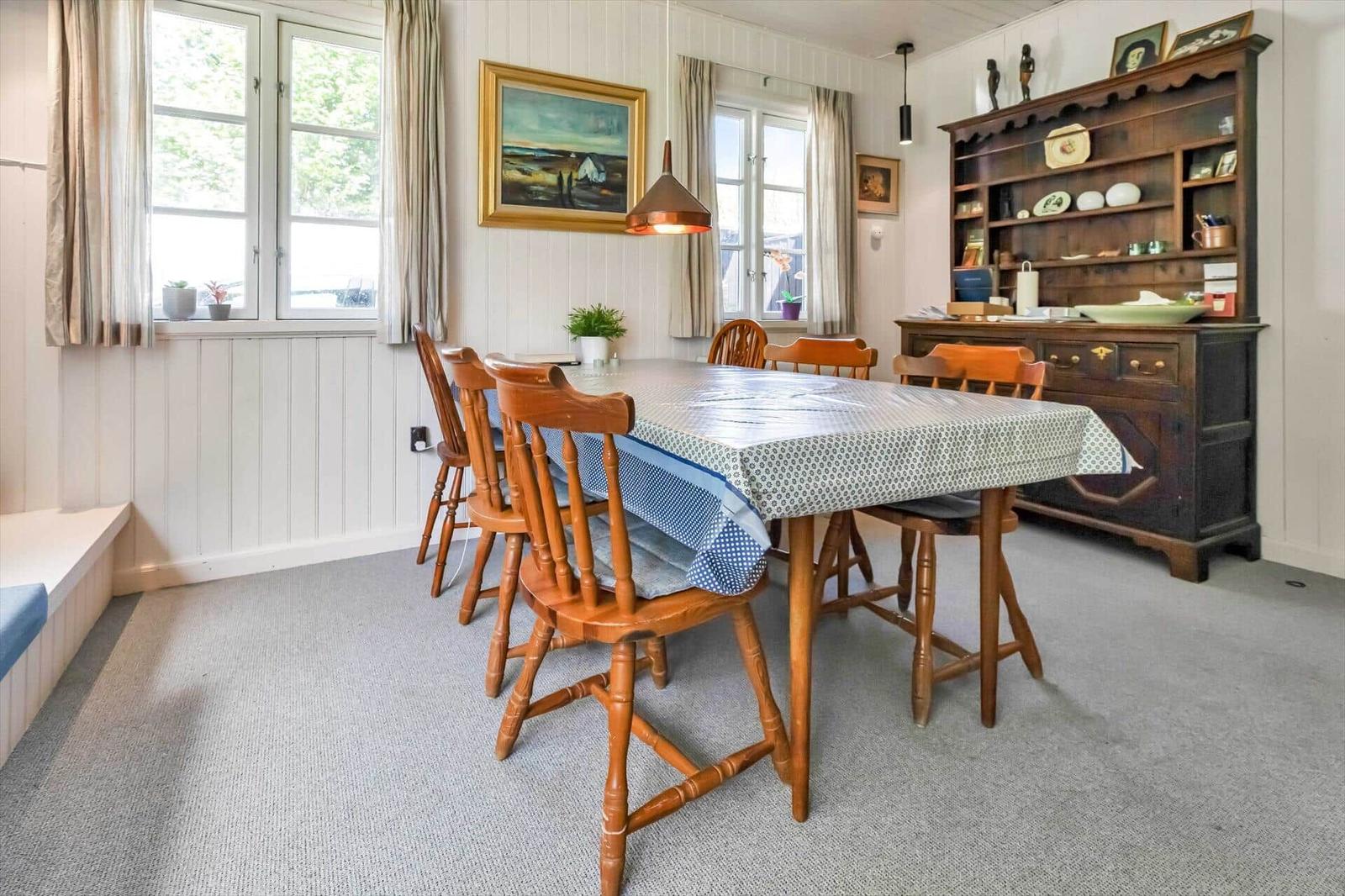 Esszimmer mit Holztisch, Stühlen und Schrank. Fenster, Wandbilder und Teppichboden.