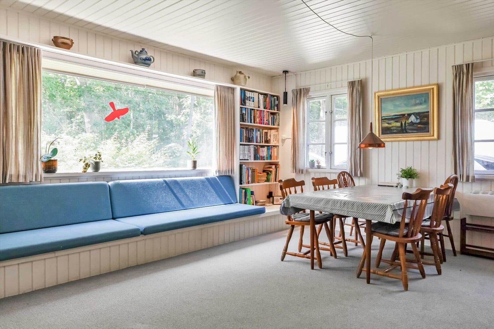 Ein Raum mit blauer Sitzbank, Essbereich und Bücherregal an der Wand.