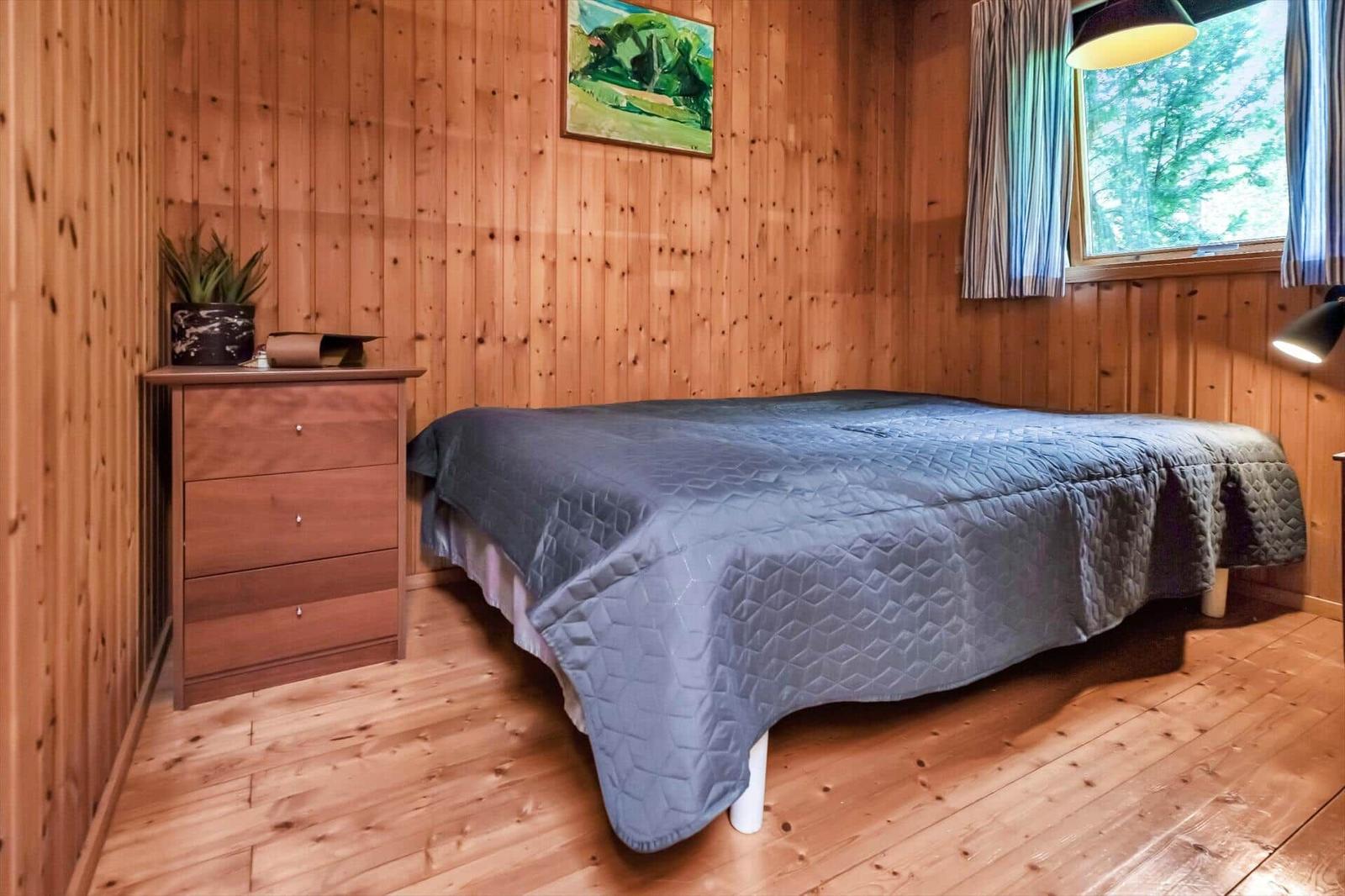 Schlafzimmer mit Holzwand, Bett, Schrank und Fenster mit Blick auf Wald.