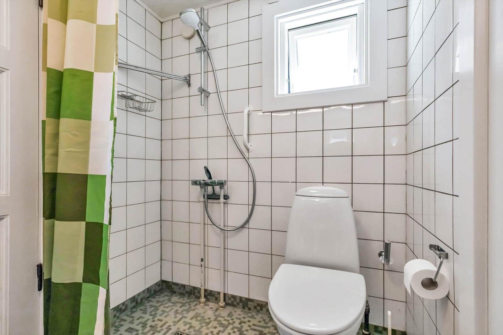 Badezimmer mit Dusche, WC und Fenster. Duschvorhang mit grün-weißem Muster.