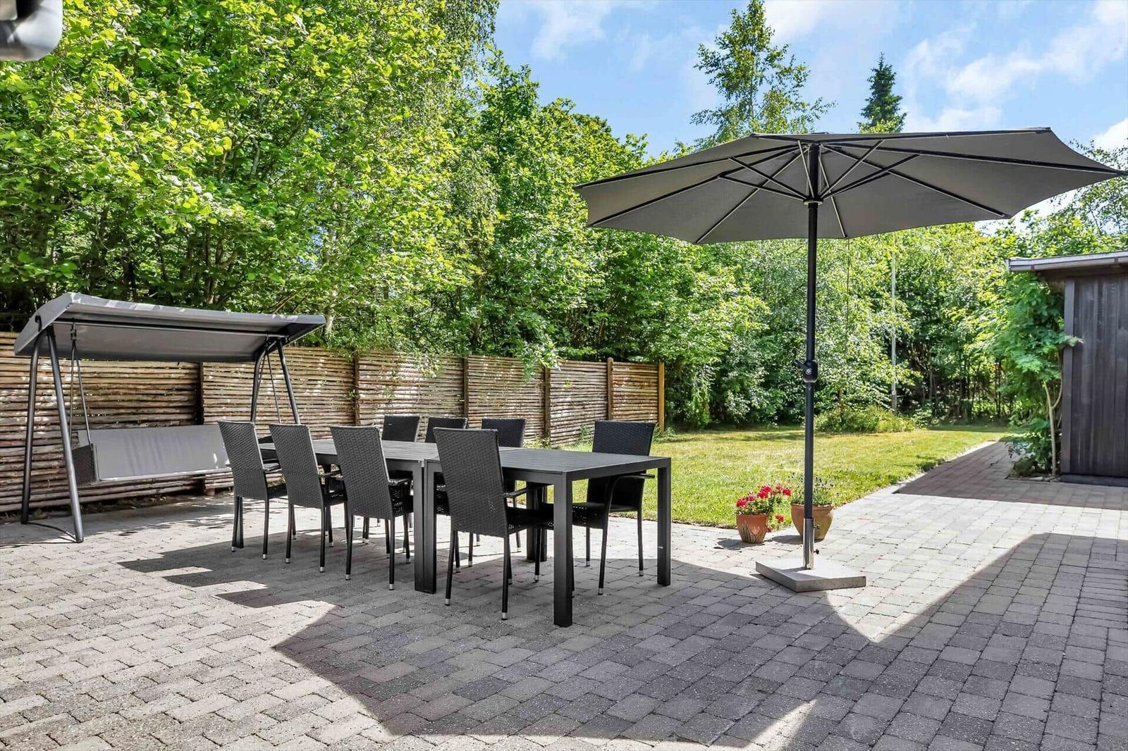 Garten mit Tisch, Stühlen, Sonnenschirm und Schaukel unter Bäumen.