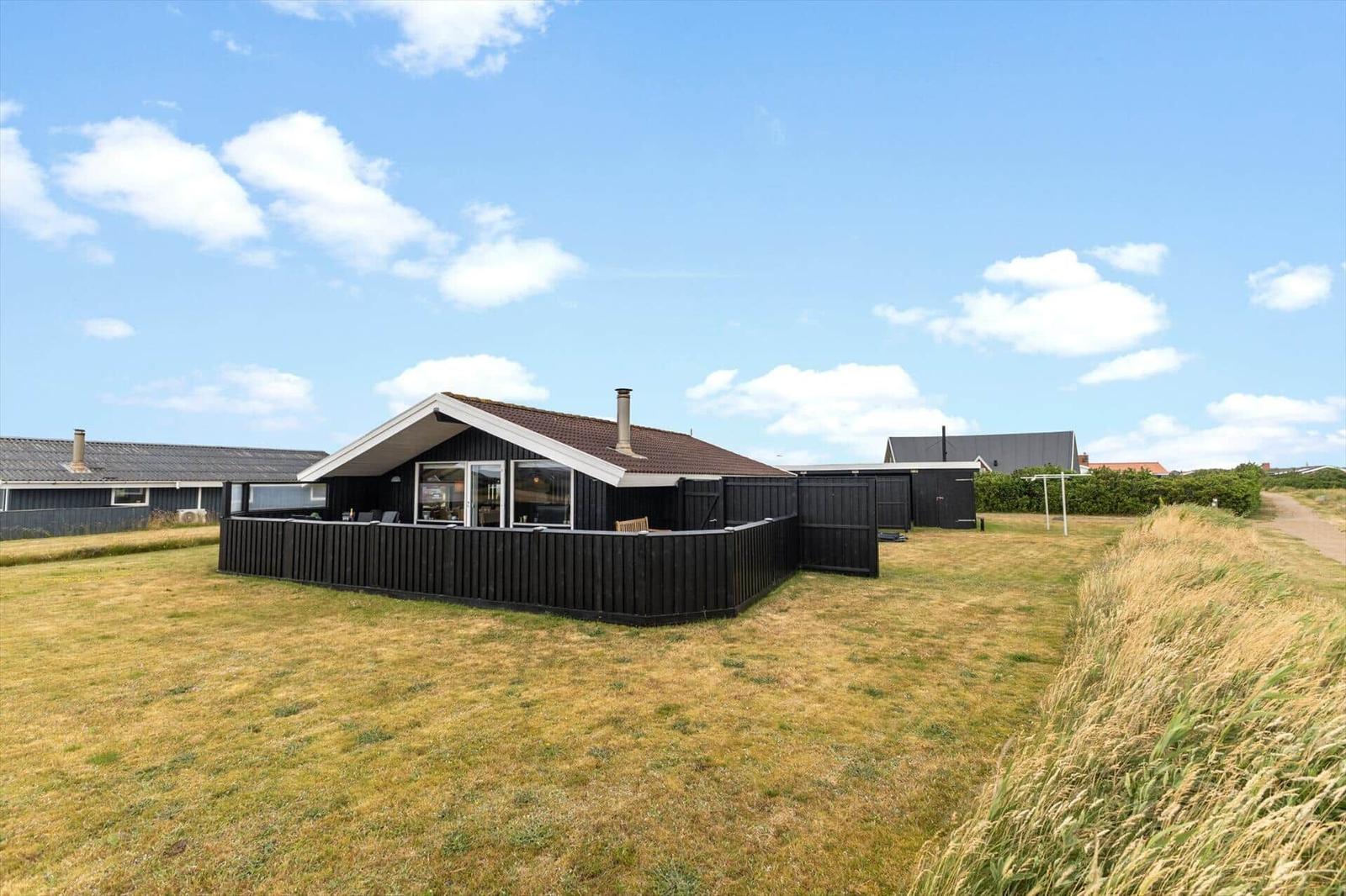 Ein modernes Haus mit großem Garten und Terrasse unter blauem Himmel.