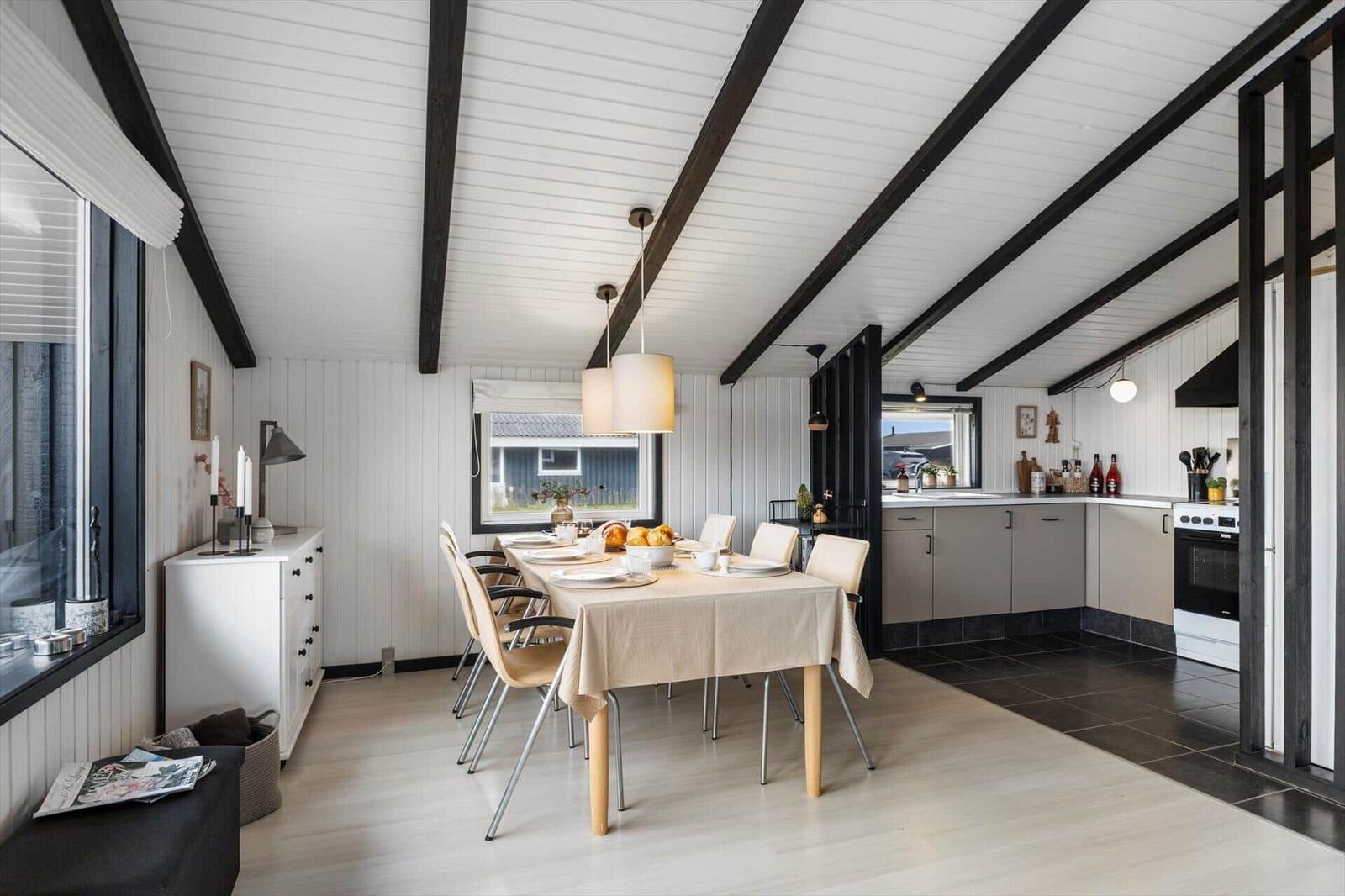 Essbereich mit Tisch und Stühlen, Küche mit Arbeitsfläche und Herd, weißer Holzdeckenrahmen.