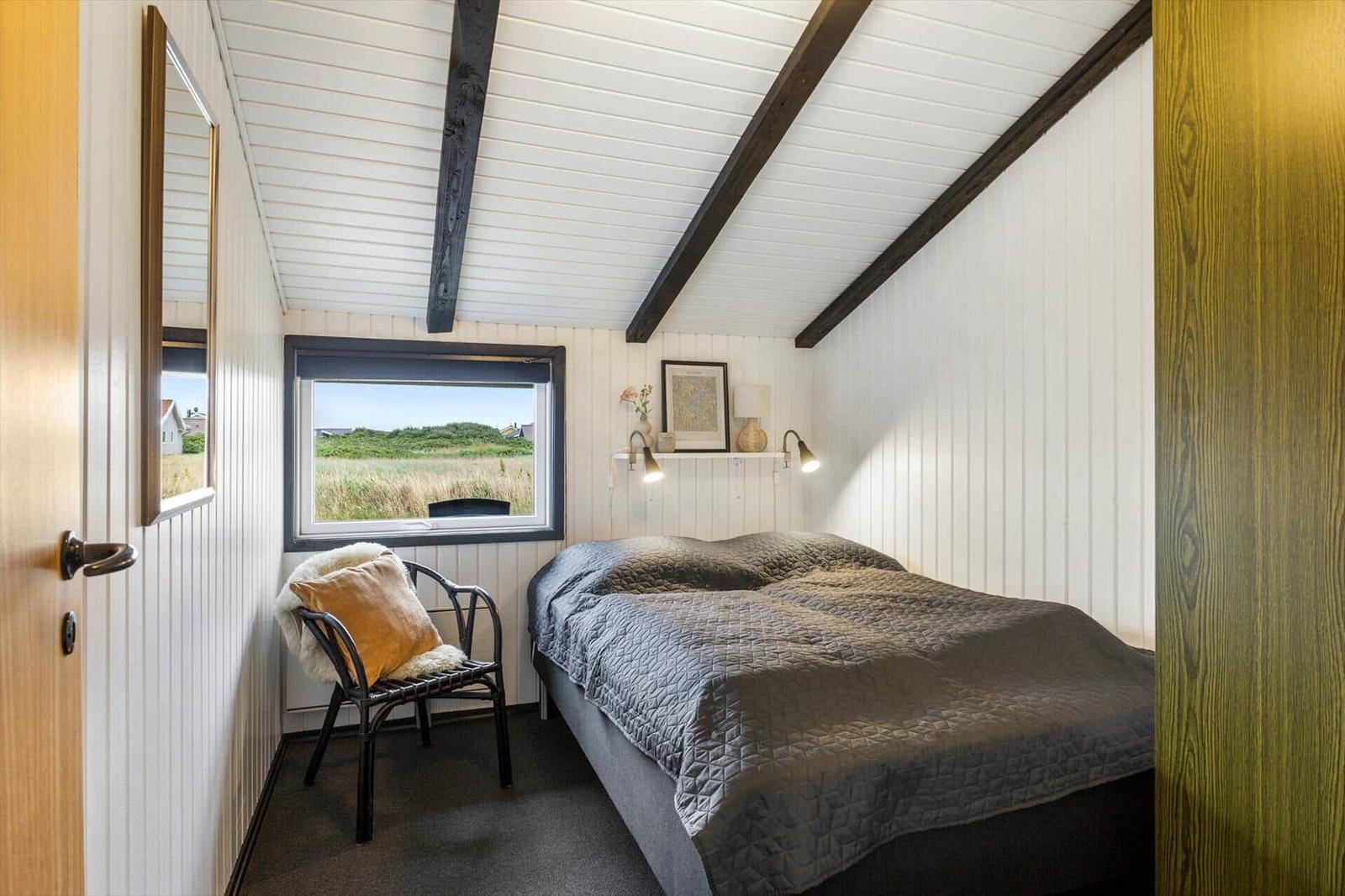 Schlafzimmer mit Bett, Stuhl und Fensterblick auf Grasland.