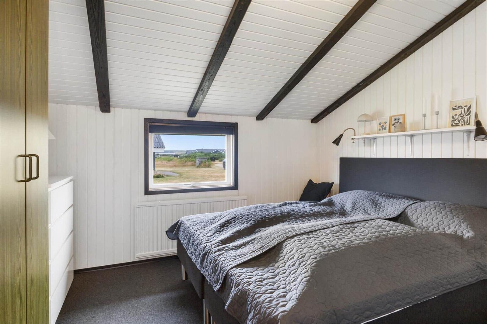 Schlafzimmer mit Bett, Fenster und Holzbalken an der Decke.