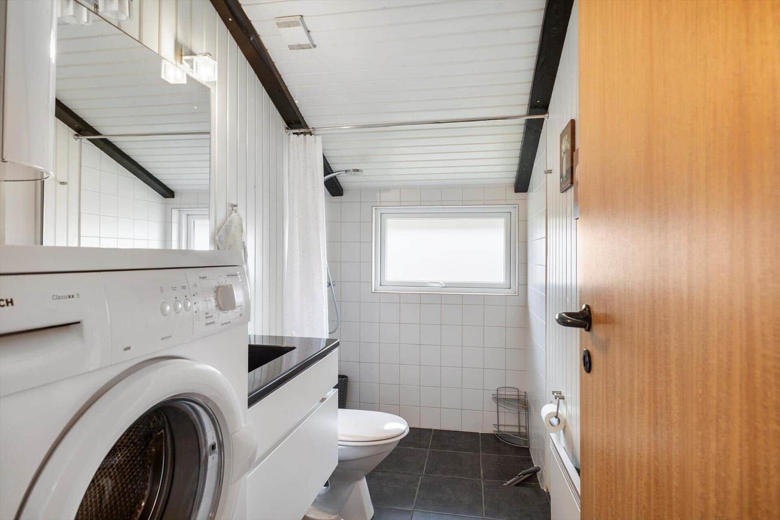 Badezimmer mit Waschmaschine, Toilette und Dusche. Weiße Fliesen und Holztür.