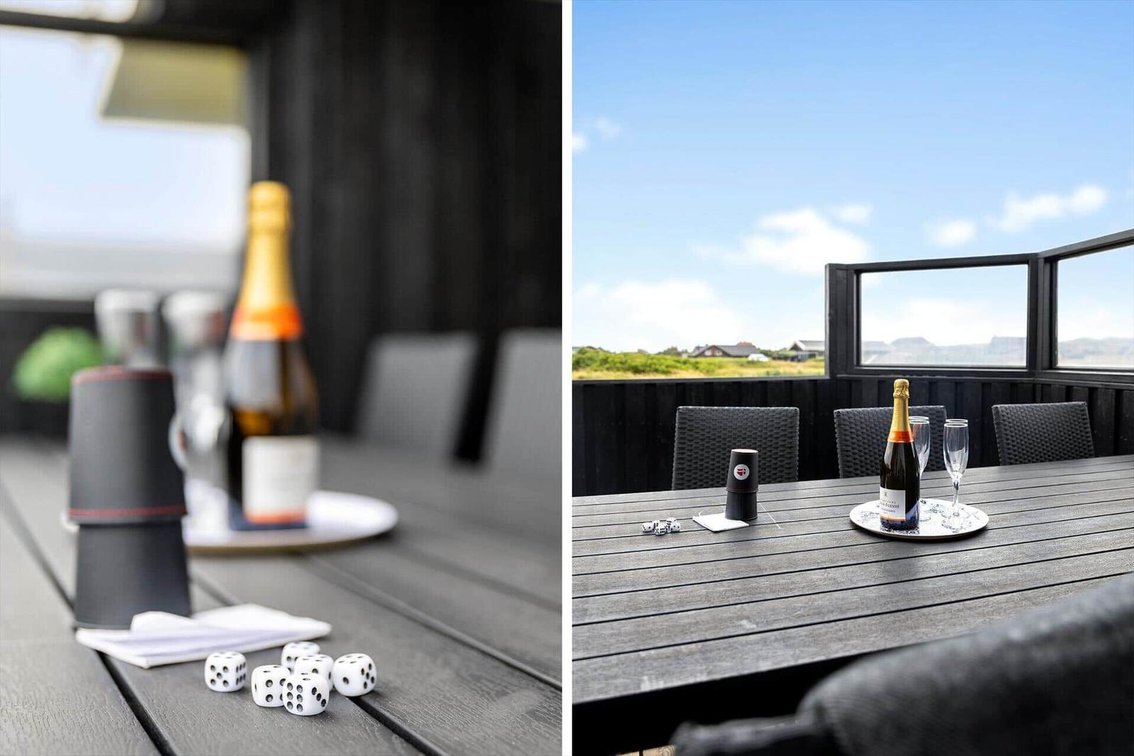 Terrasse mit Tisch, Stühlen und Champagner. Blick auf Landschaft und Himmel.