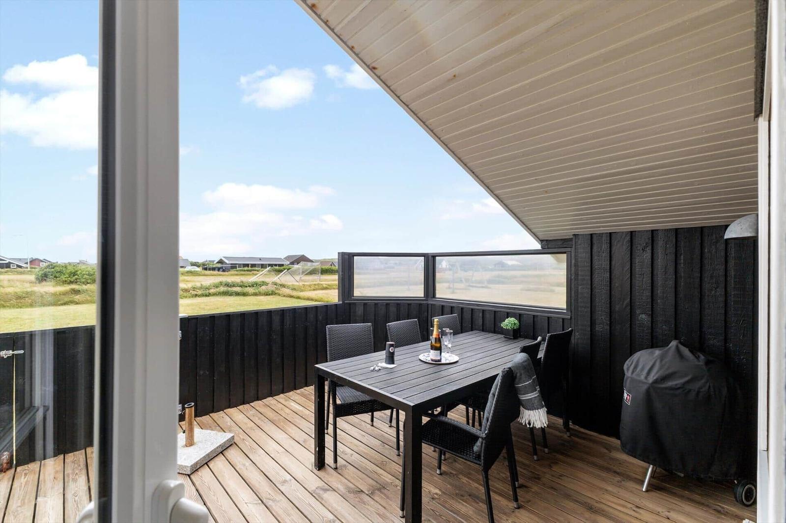 Terrasse mit Tisch, Stühlen und Grill. Blick auf grüne Landschaft und Himmel.
