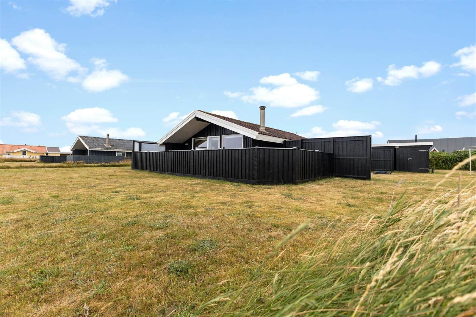 Ein modernes Haus mit schwarzem Zaun und Dach, umgeben von Grasland unter blauem Himmel.