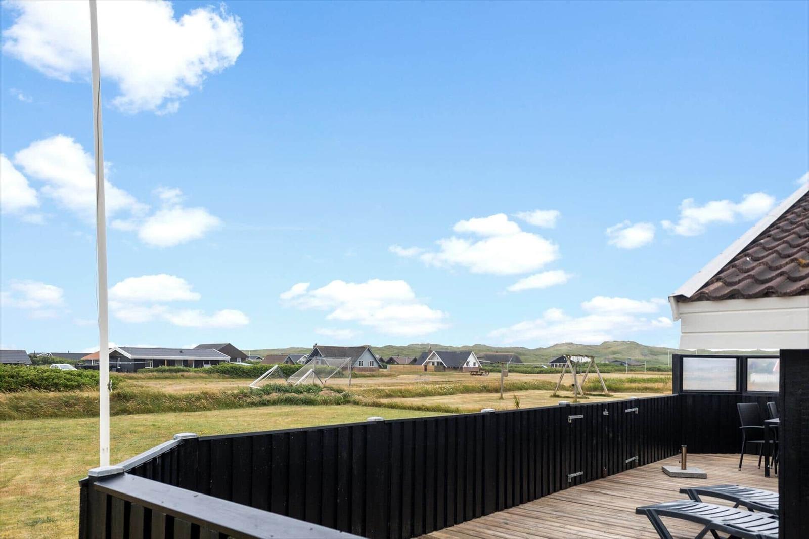 Terrasse mit Blick auf grünes Feld und Häuser im Hintergrund unter blauem Himmel.
