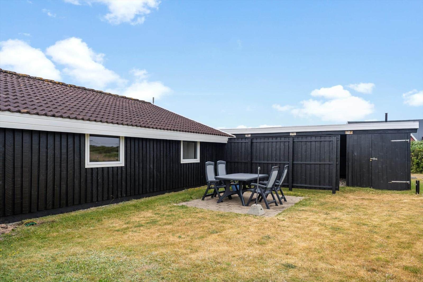 Haus mit Garten, Sitzgruppe und Schuppen. Helle Fenster und braune Dachziegel.