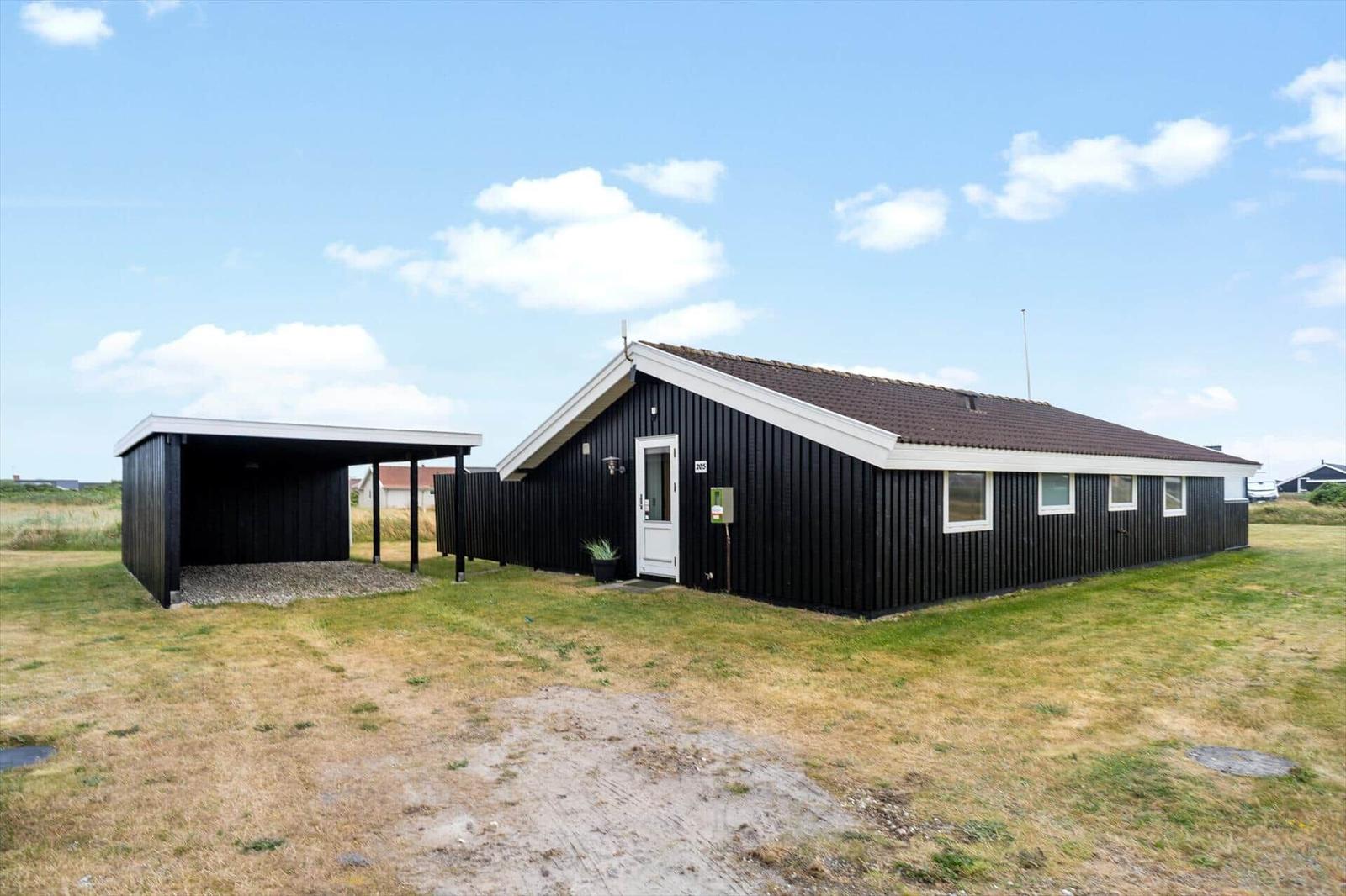 Schwarzes Holzhaus mit Garage und Grasfläche unter blauem Himmel.