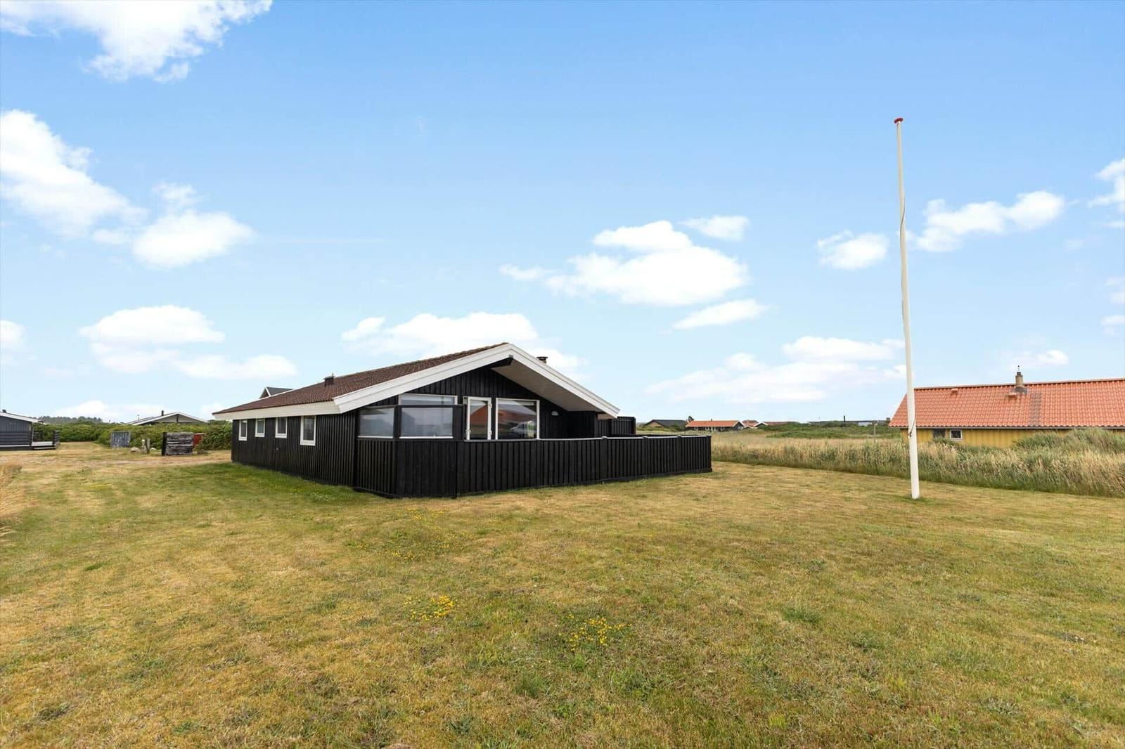 Schwarzes Holzhaus mit Terrasse auf grünem Grundstück unter blauem Himmel.