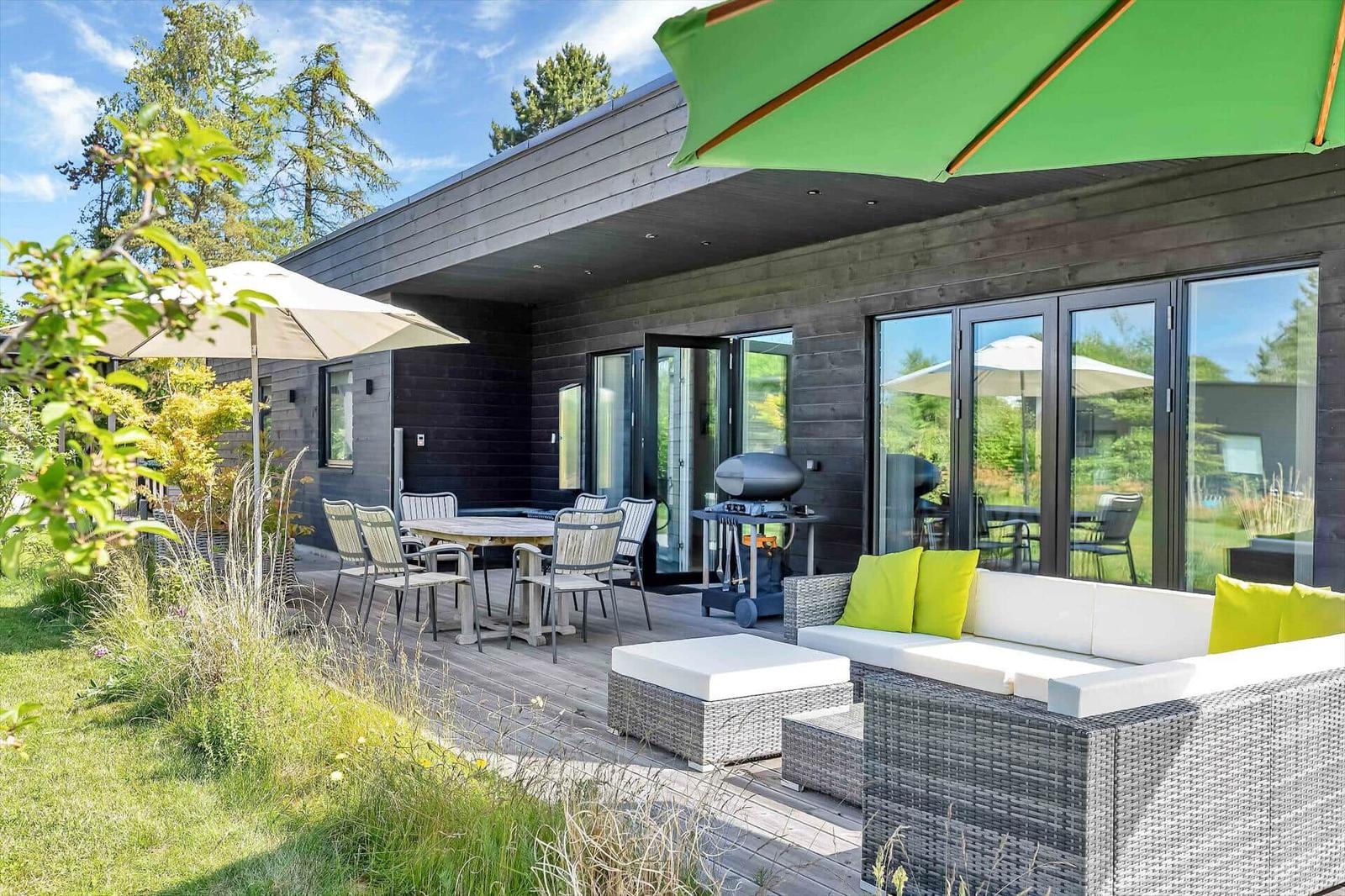 Deck with seating, table, grill, and umbrellas. Modern house with glass doors.