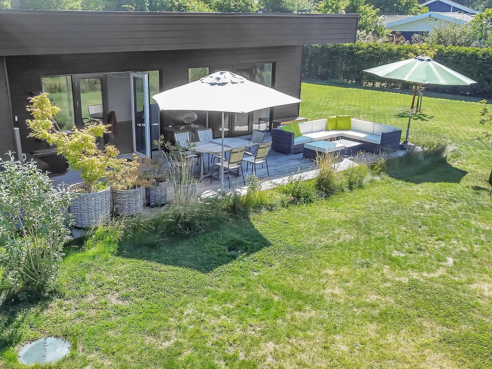 Terrace with seating area, table, and umbrella. Lawn and plants surround the terrace.