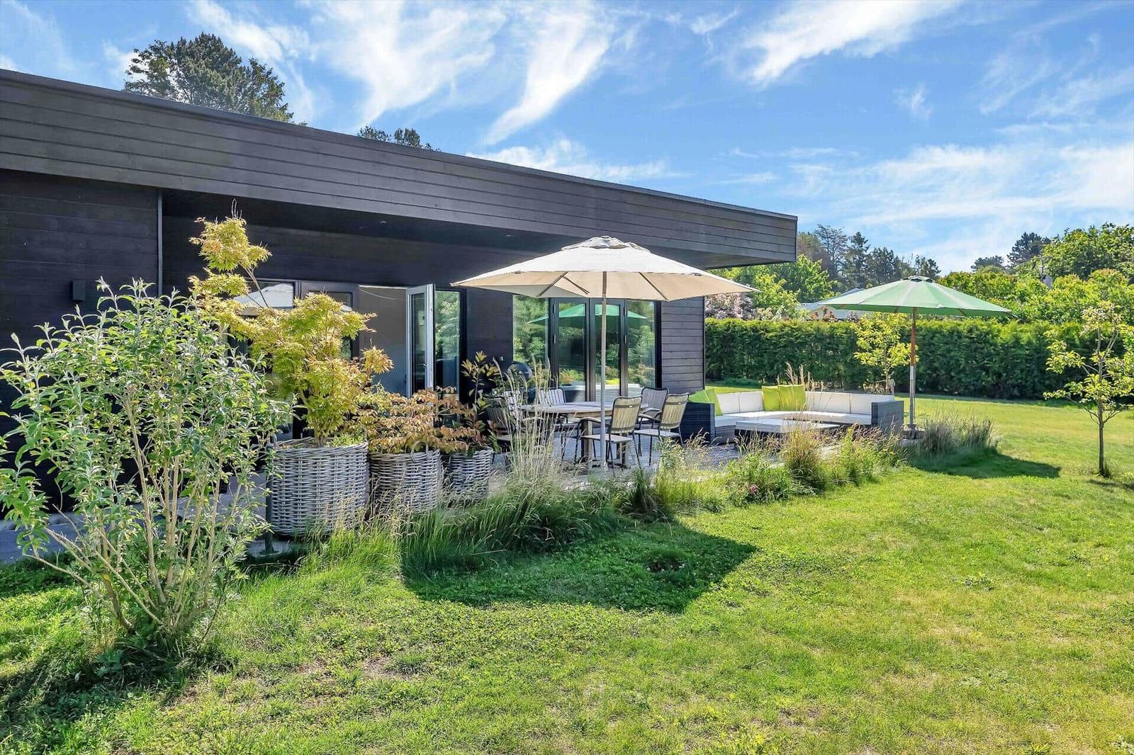 Modern villa with large garden, terrace, and seating areas under umbrellas.