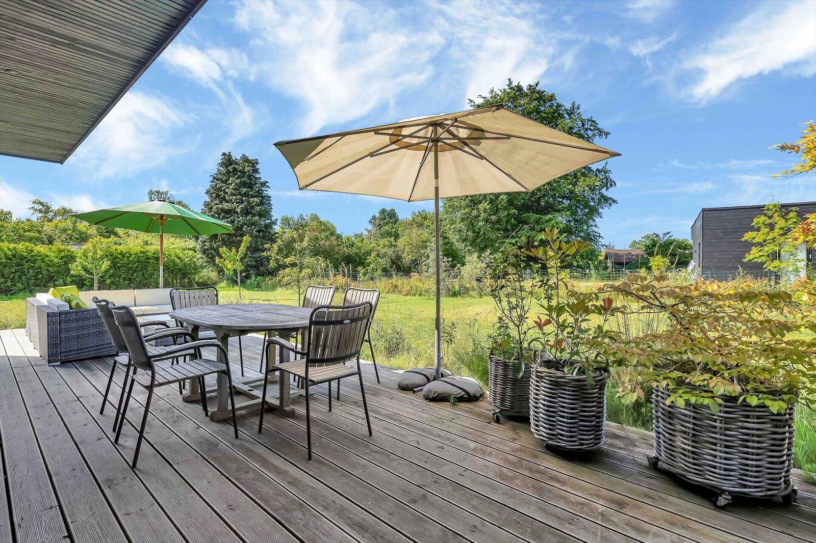 Deck with table, chairs, and umbrellas. Green fields and trees in the background.