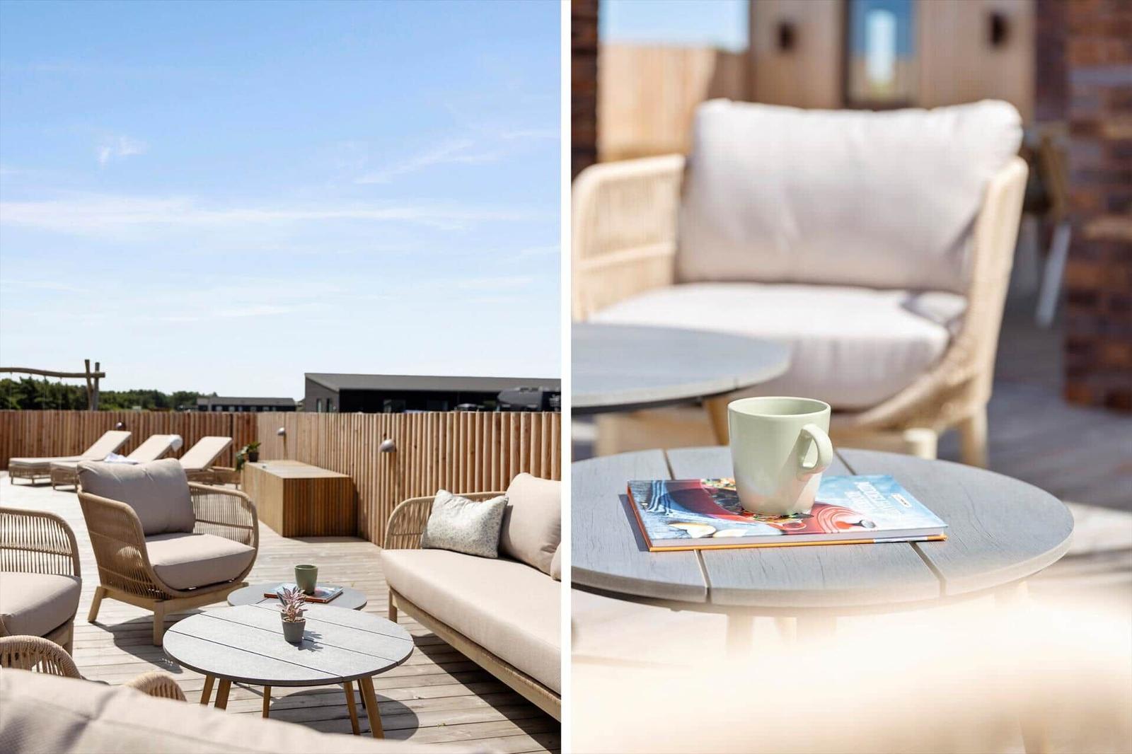 Terrasse mit Sitzgelegenheiten und Tisch. Hintergrund: Holzgeländer und blauer Himmel.