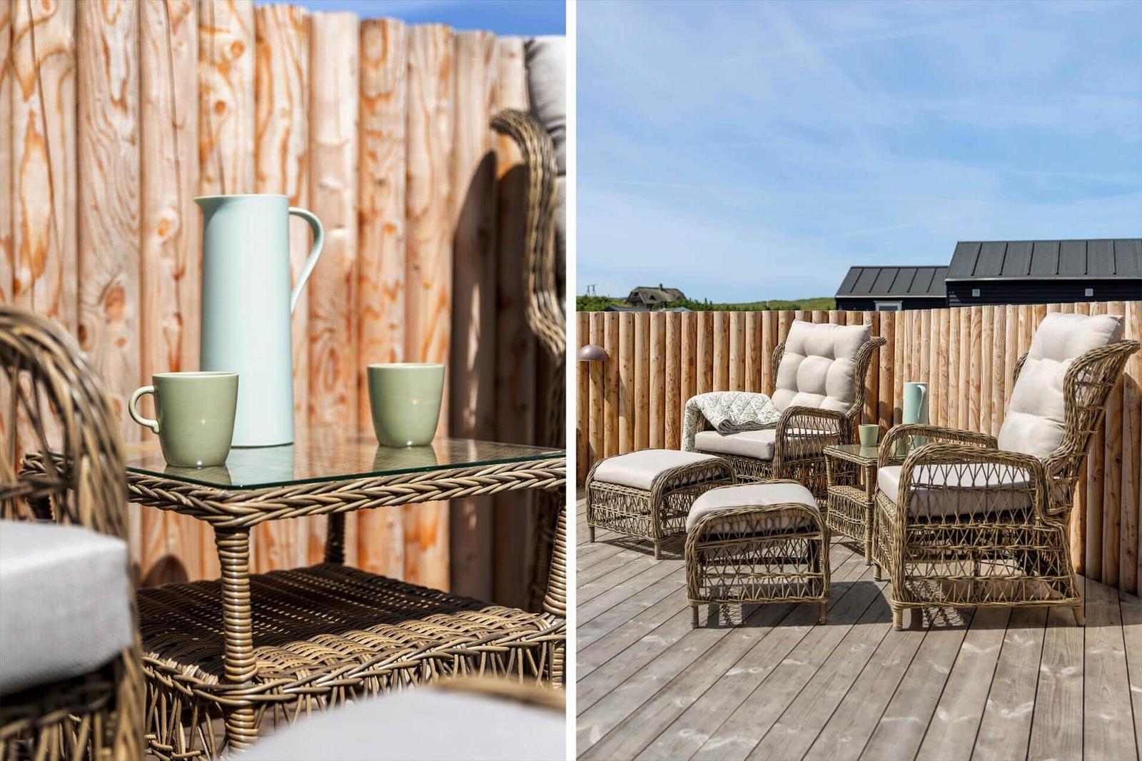 Terrasse mit Rattanmöbeln, GlasTisch und Holzgeländer. Hintergrund: Holzwand und blauer Himmel.
