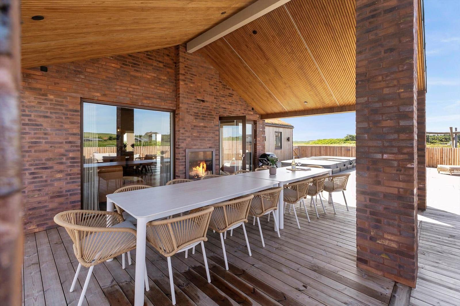 Terrasse mit Esstisch, Sitzgelegenheiten und Kamin. Holzdecke und Ziegelmauer.