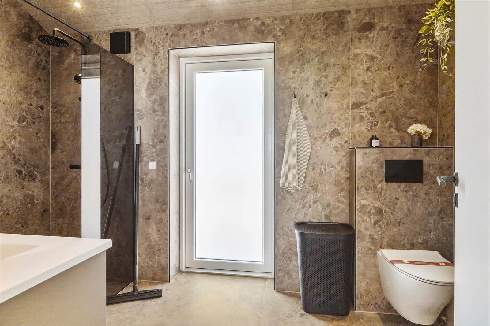Badezimmer mit Dusche, Toilette und Fenster. Wände und Boden sind aus Stein.