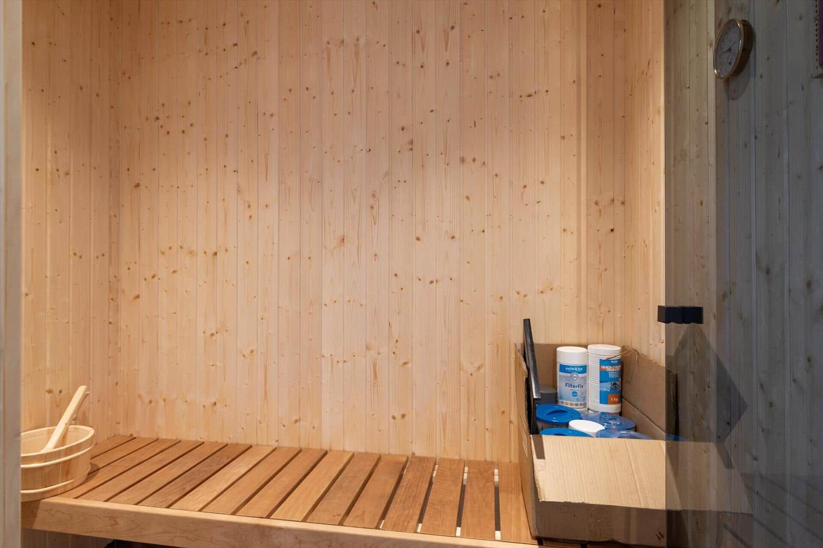 Sauna mit Holzwand, Sitzbank, Eimer und Reinigungsmittel.