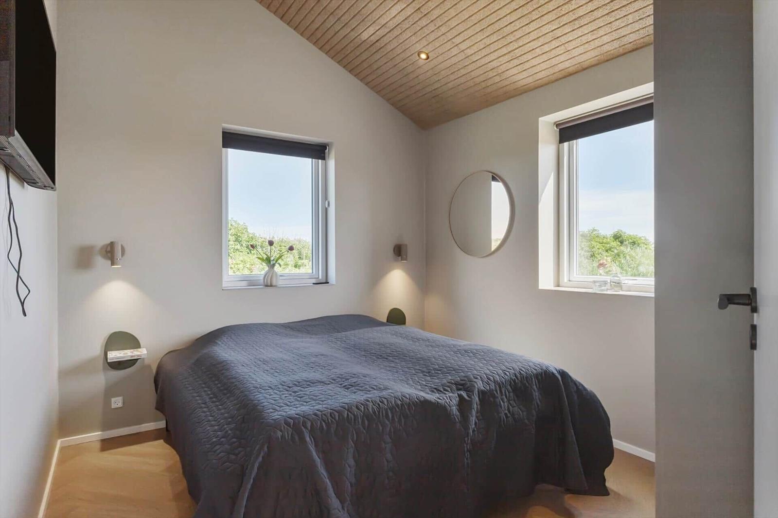 Schlafzimmer mit Bett, zwei Fenstern und runden Wandspiegeln.