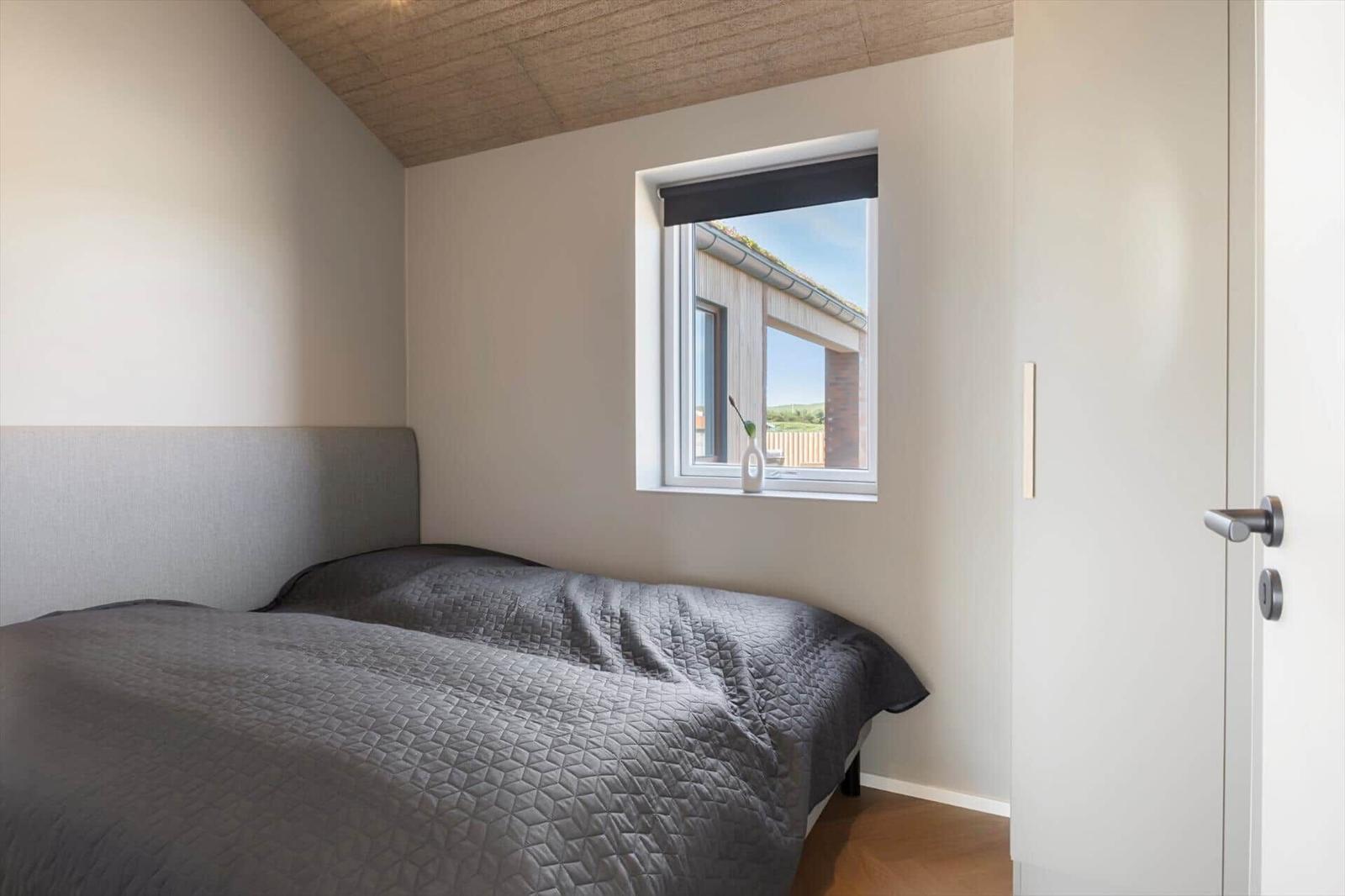 Schlafzimmer mit Bett, Fenster und Holzdecke.
