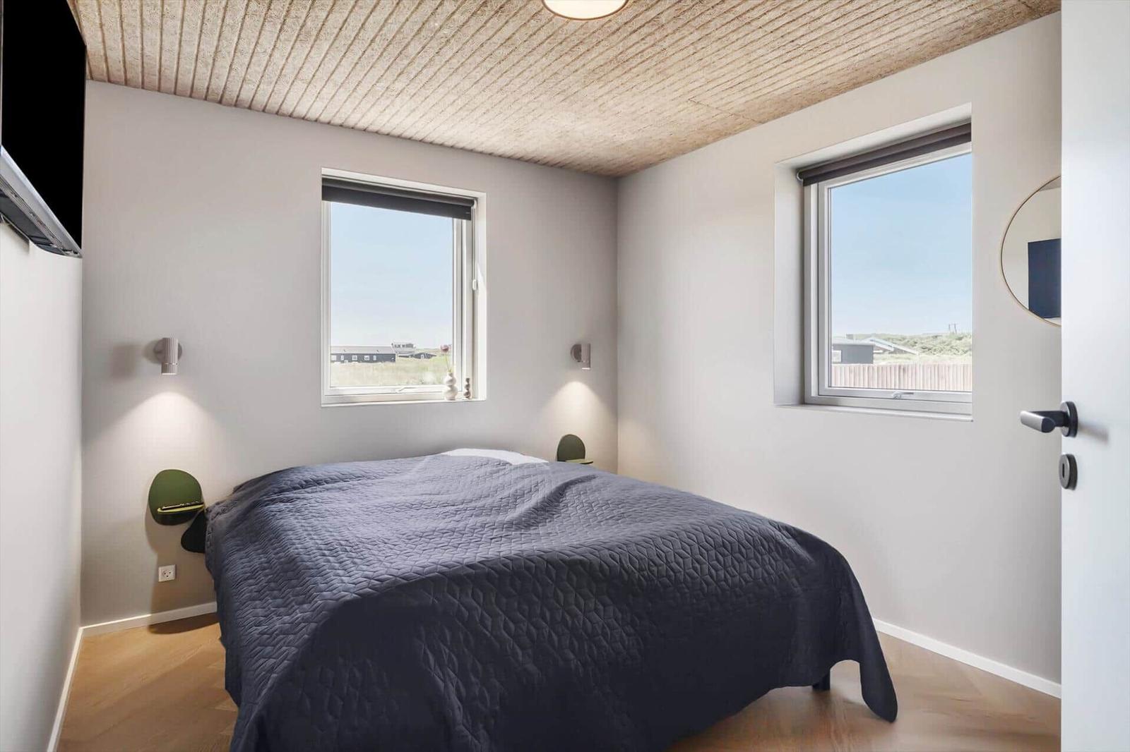 Schlafzimmer mit Bett, zwei Fenstern und Holzboden. Decke aus Holzdielen.