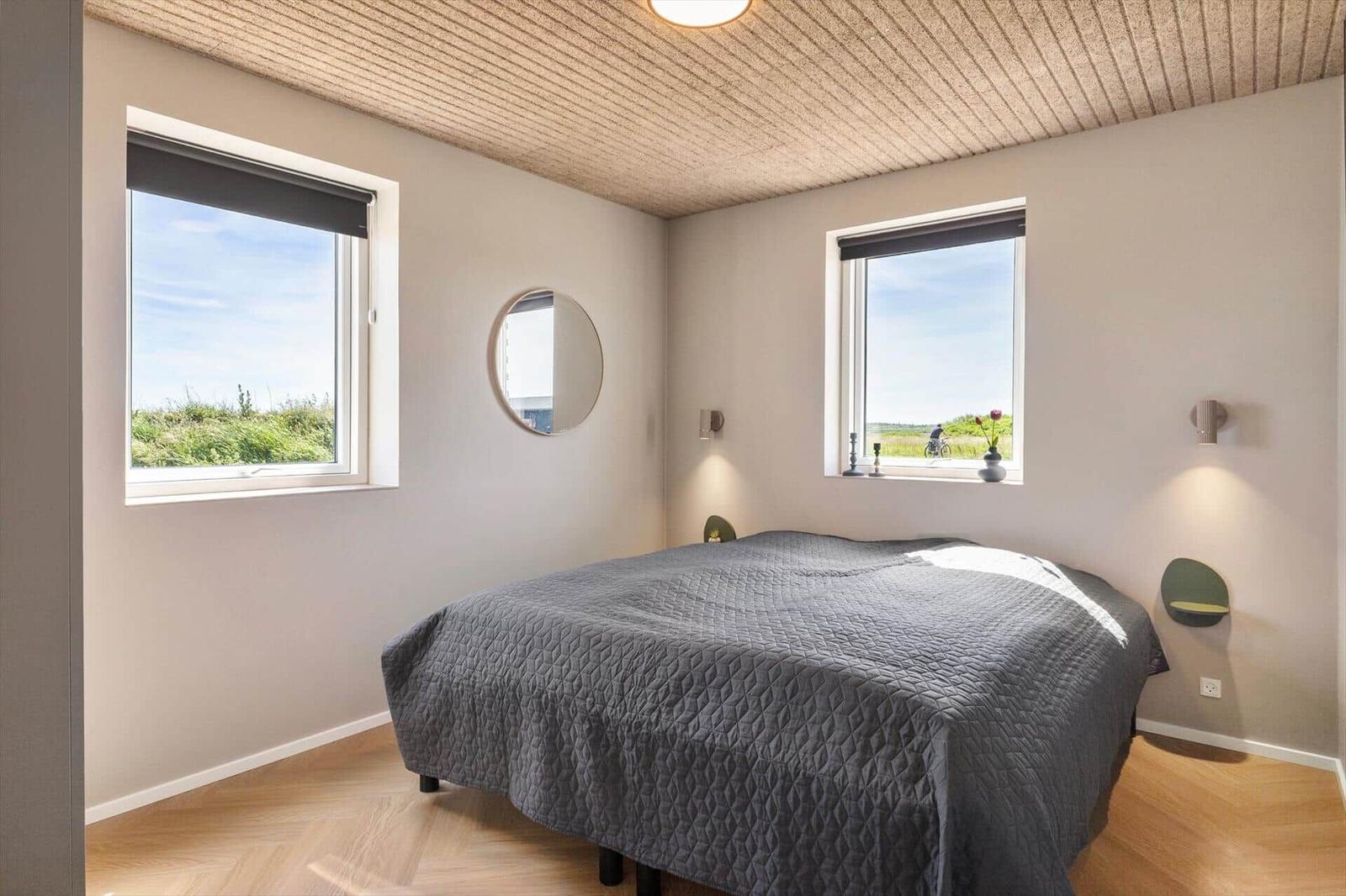 Schlafzimmer mit Doppelbett, zwei Fenstern und runden Spiegeln an den Wänden.