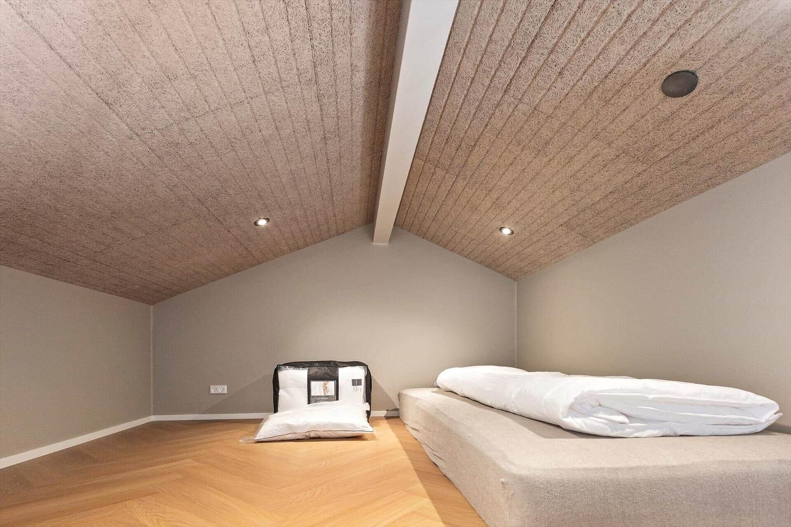 Schlafzimmer mit Bett, Holzboden und schrägem Dach mit eingebauten Lichtern.
