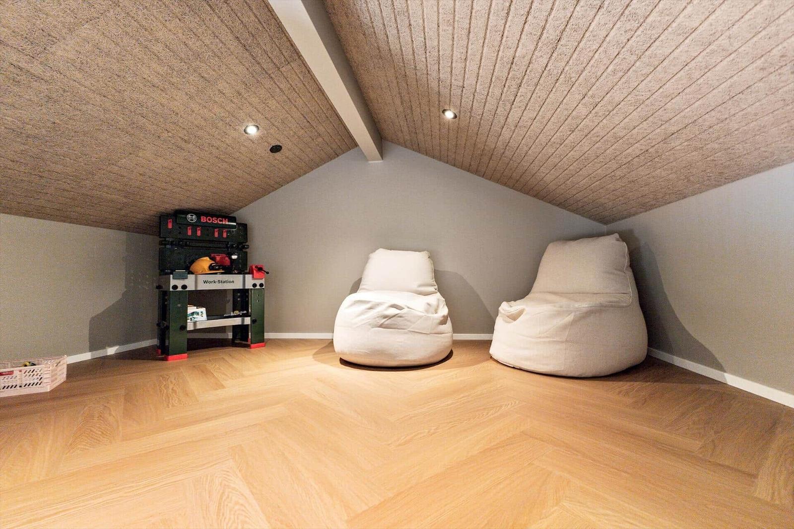 Zwei weiße Sitzgelegenheiten und eine Werkbank im Dachbodenraum mit Holzboden und Holzdecke.