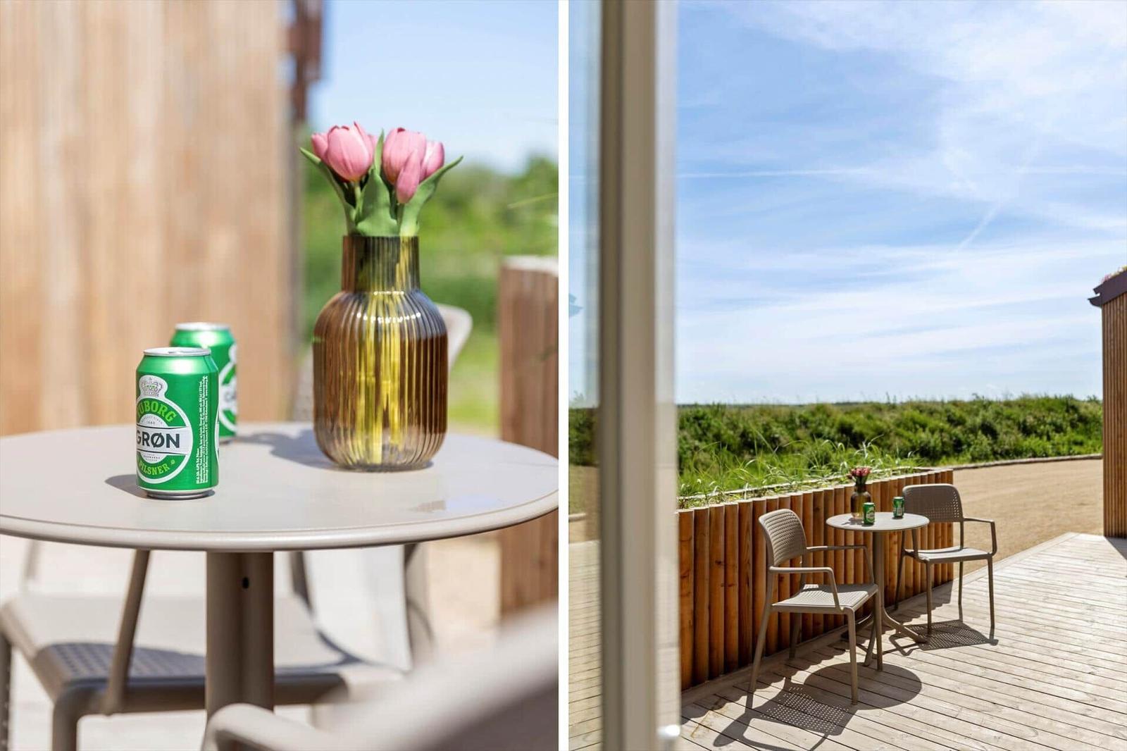 Terrasse mit Tisch, Stühlen und Blumen. Blick auf grünes Feld unter blauem Himmel.