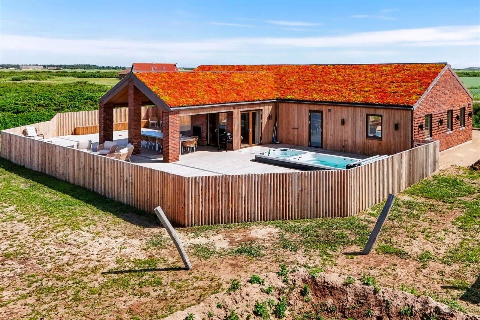 Moderne Villa mit Holzfassade und rotem Dach, umgeben von einer Terrasse mit Pool und Garten.
