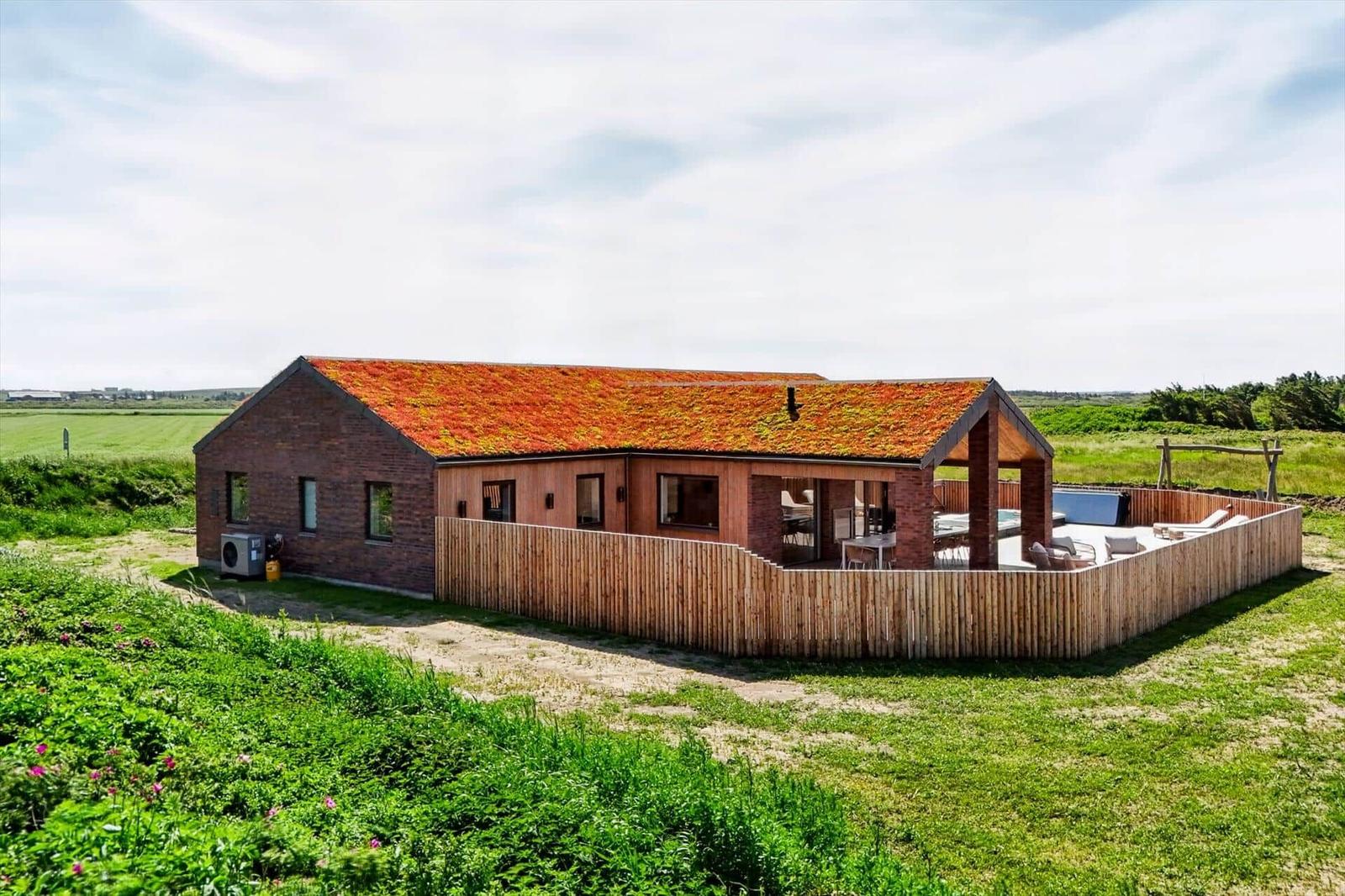 Moderne Villa mit grüner Dachdeckung, Holzterrasse und Garten. Poolbereich mit Liegestühlen.