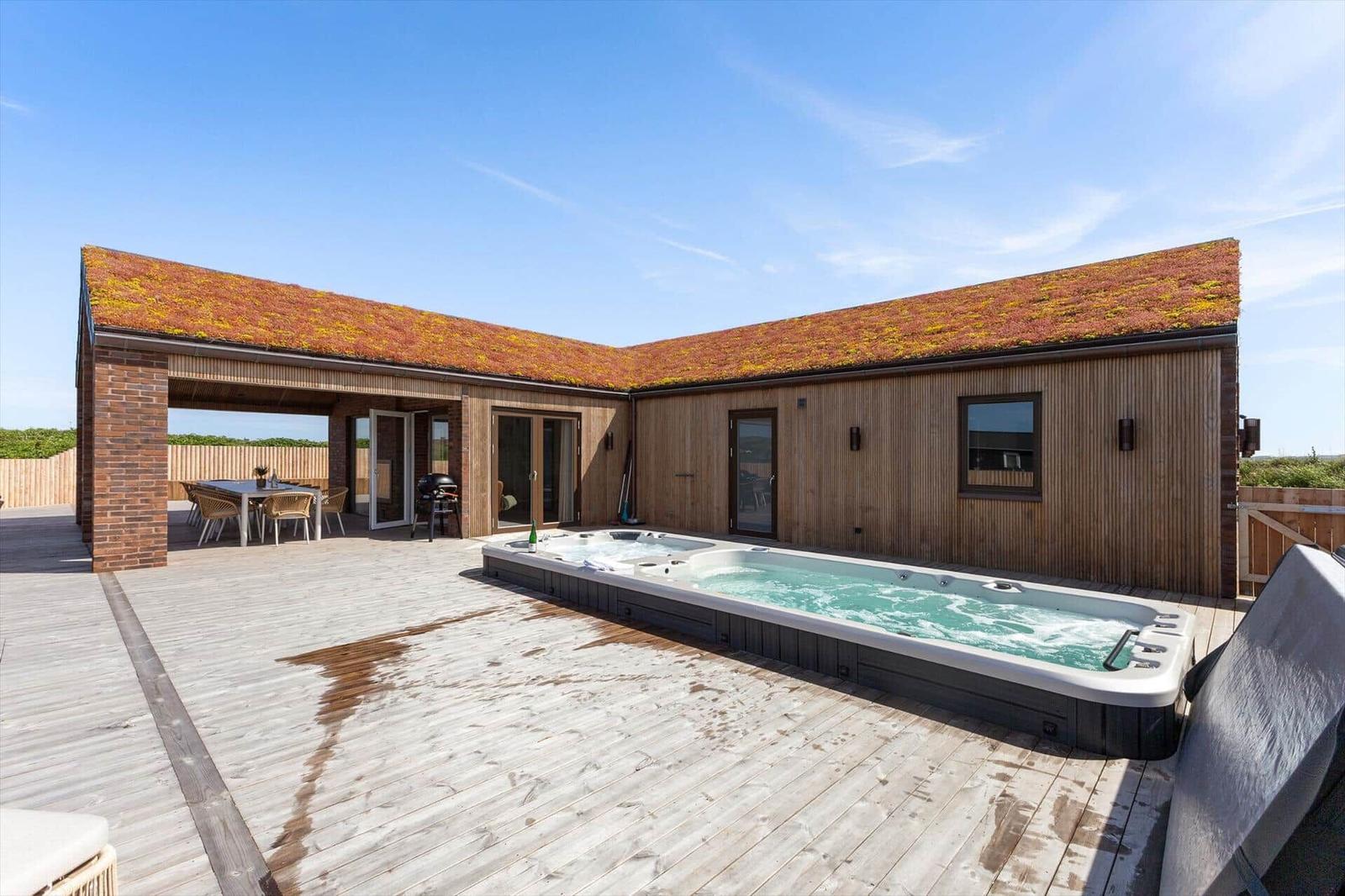 Moderne Villa mit Whirlpool, Holzterrasse und grüner Dachfläche.