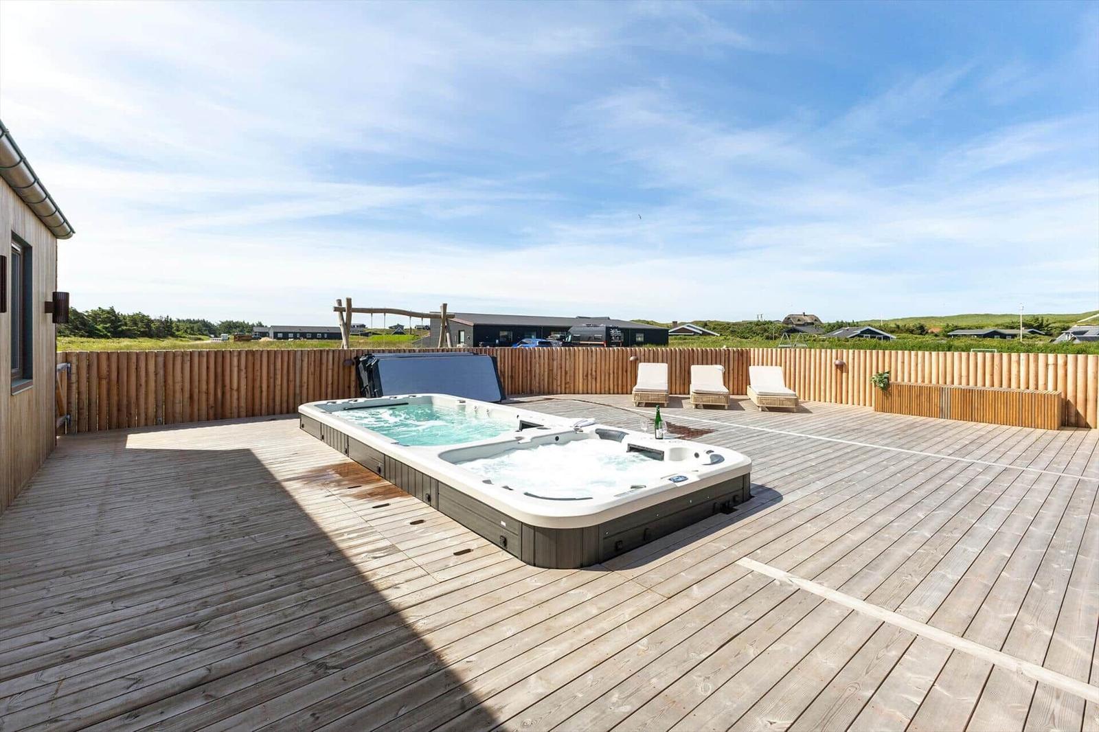 Terrasse mit Whirlpool und Liegen, umgeben von Holzzaun und Grünland.