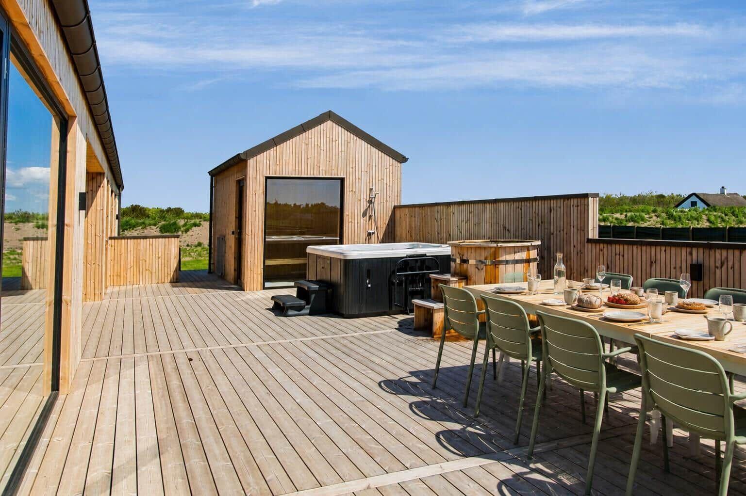 Terrasse mit Hot Tub, Esstisch und Holzhaus im Hintergrund.