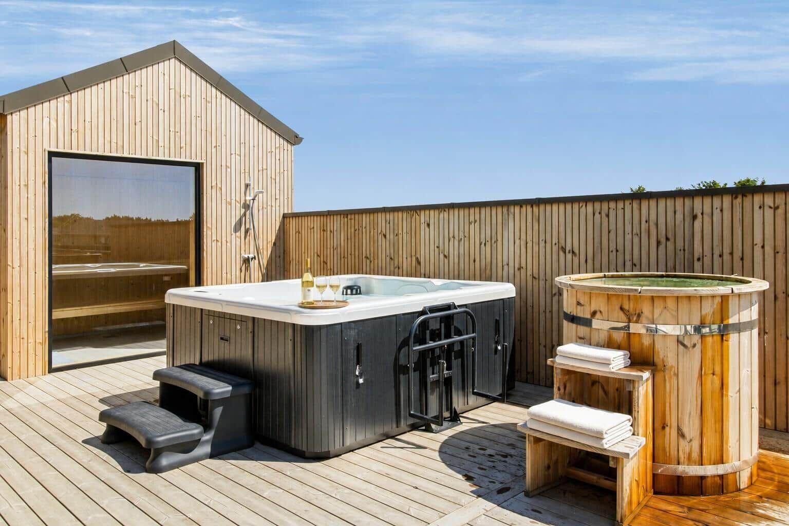 Außenbereich mit Whirlpool, Holzbad und Holzterrasse. Hintergrund: Holzhaus mit Glasfront.