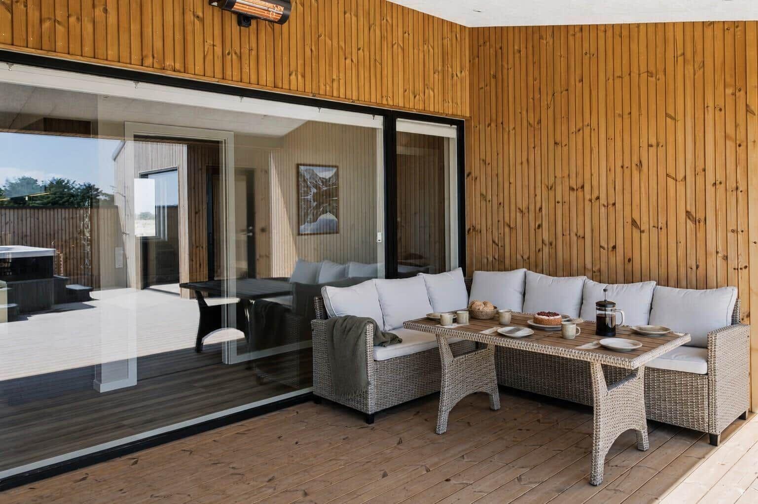 Terrasse mit Sitzgruppe und Tisch. Holzwände und Glasfront. Im Hintergrund Blick in das Haus.