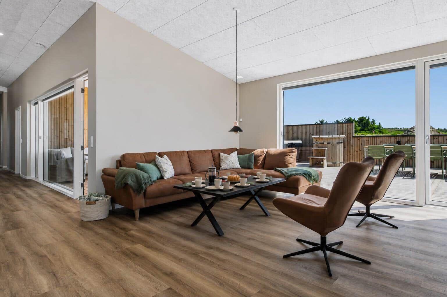 Wohnzimmer mit braunem Sofa, zwei Sesseln und Blick auf Terrasse.