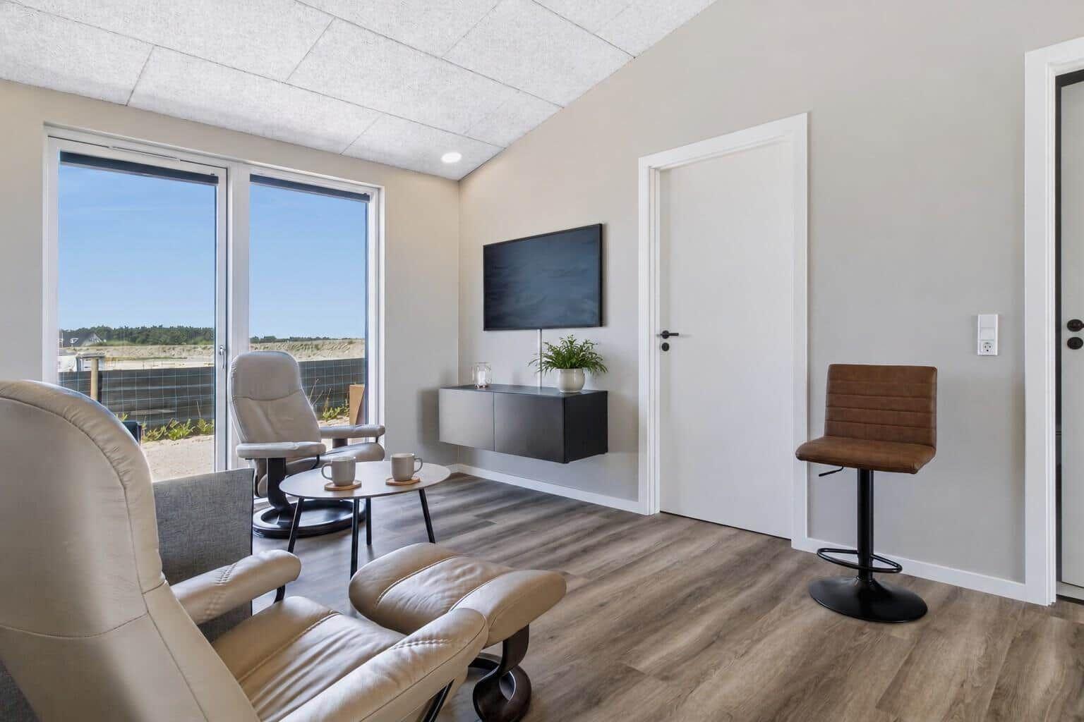 Wohnzimmer mit Sitzgelegenheiten, Fernseher und Blick auf den Außenbereich.