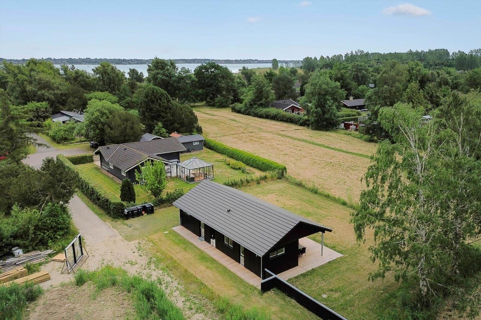 Modernes Haus mit Terrasse, umgeben von Grün und einem See im Hintergrund.
