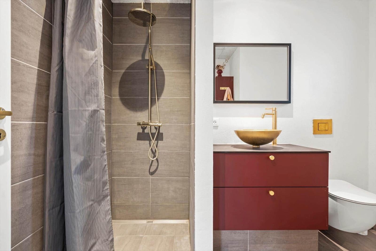 Bad mit Dusche, Waschbecken und Toilette. Rot lackierter Schrank mit goldfarbenem Waschbecken.