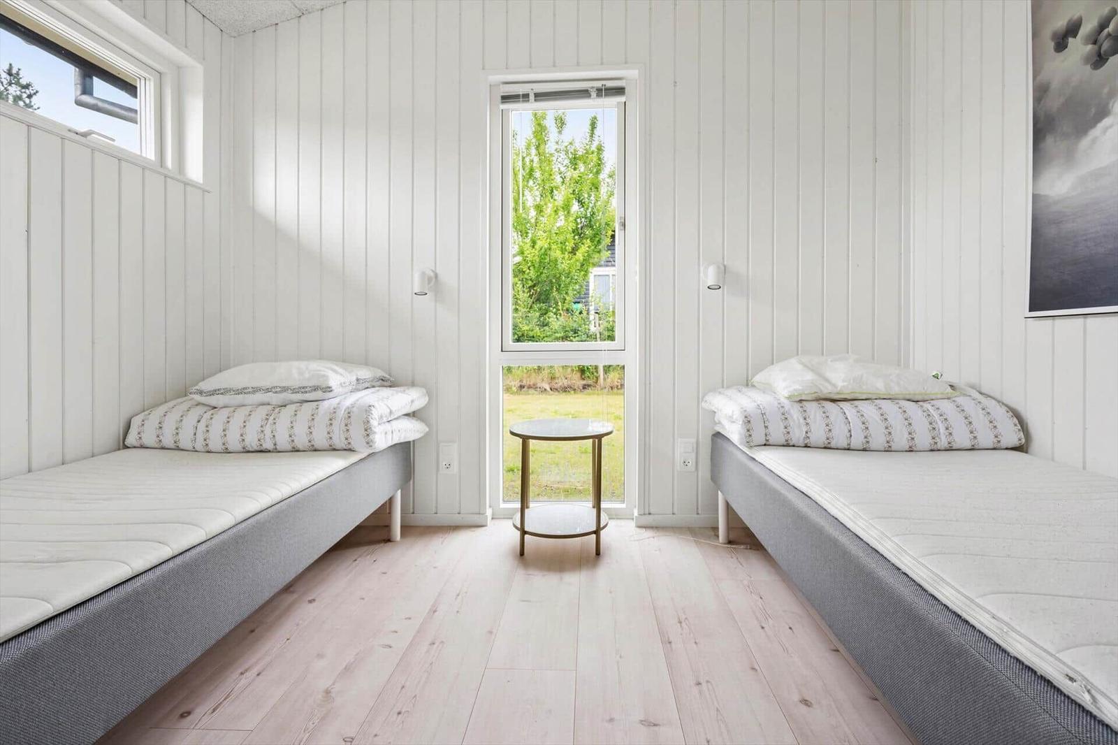 Zwei Betten mit Matratzen und Bettwäsche stehen in einem Raum mit weißen Wänden und Holzboden.