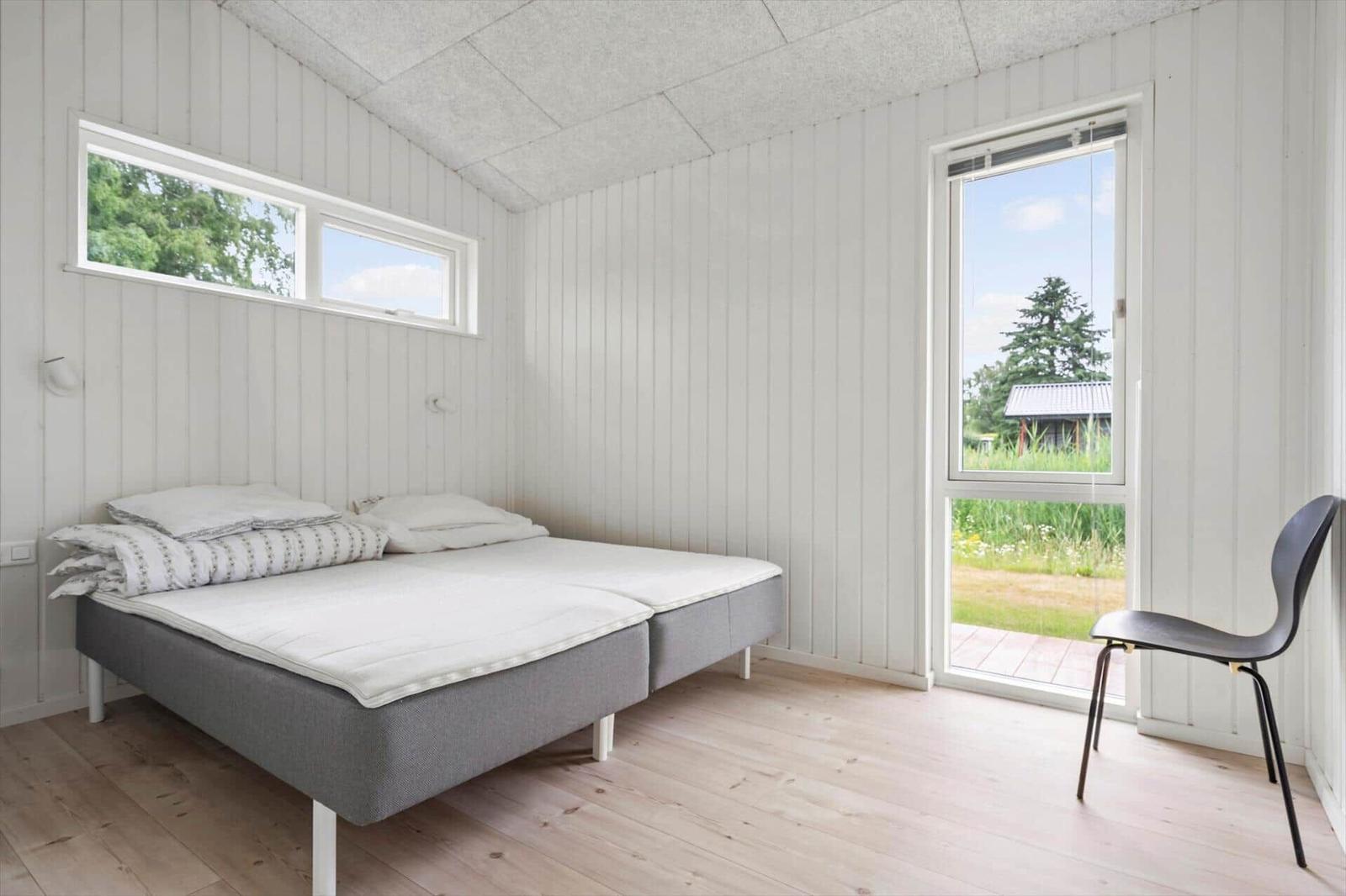 Schlafzimmer mit Bett, Stuhl und Fenstern zur Außenseite.