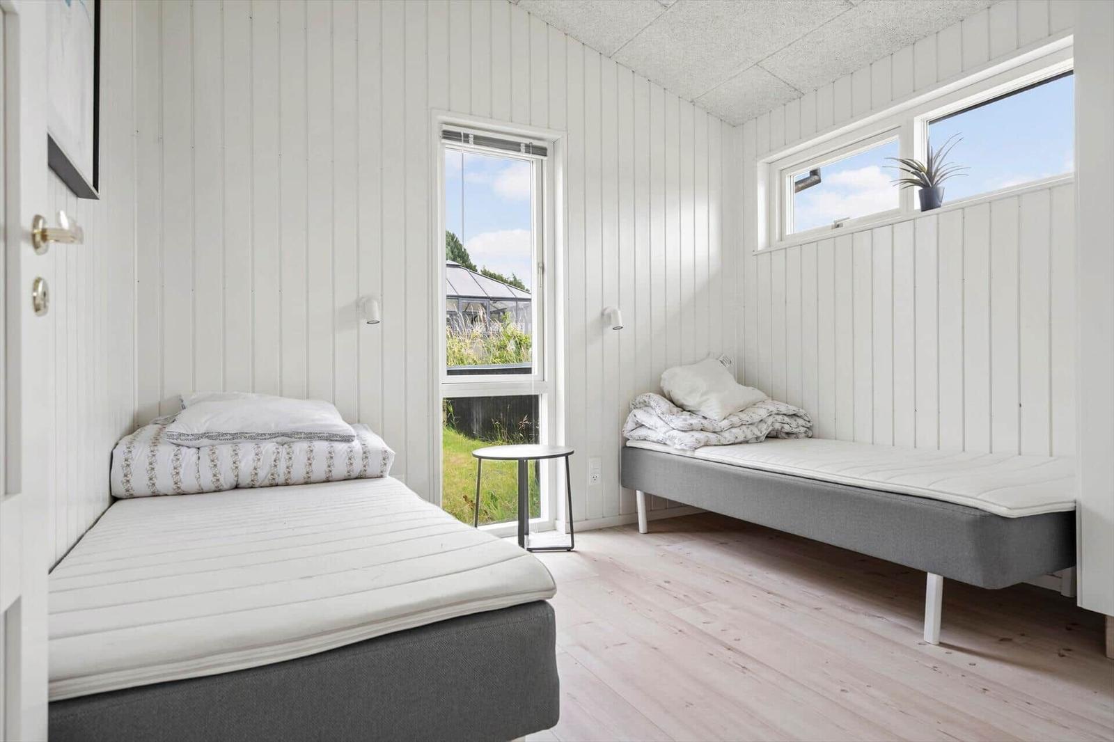 Zimmer mit zwei Betten, weißen Wänden und Fenstern mit Blick auf Gras.
