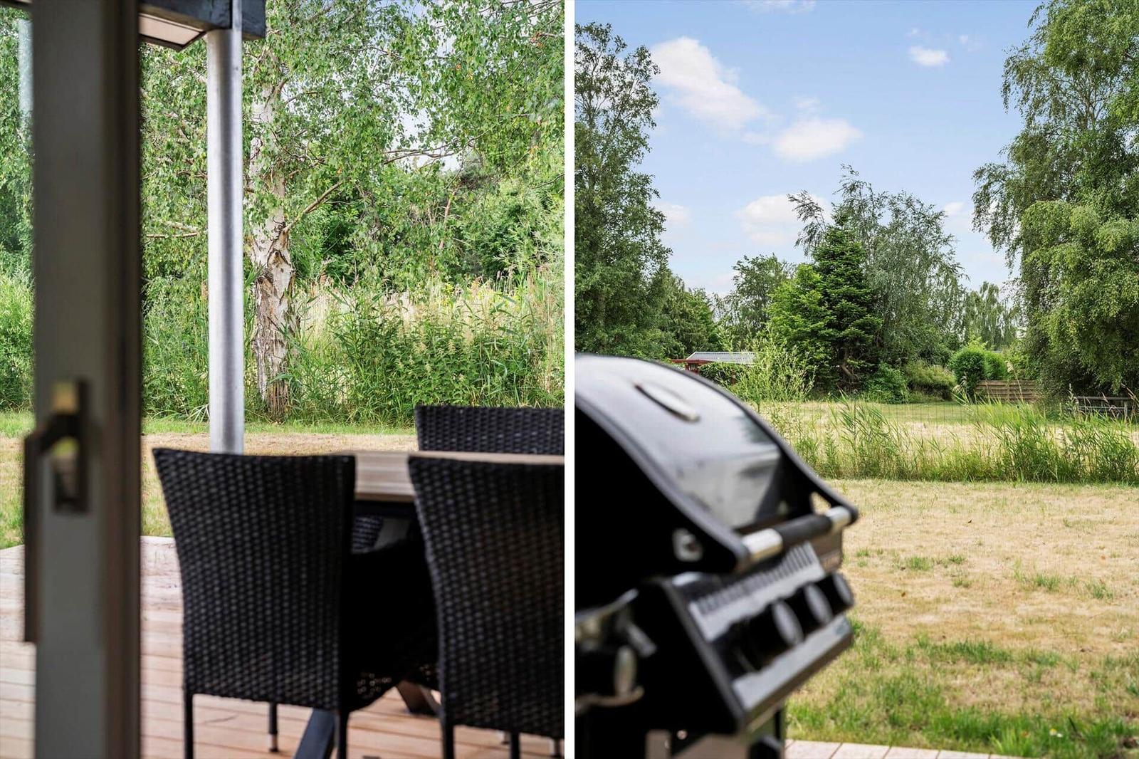 Terrasse mit Tisch und Stühlen. Grill und Grünfläche im Hintergrund.