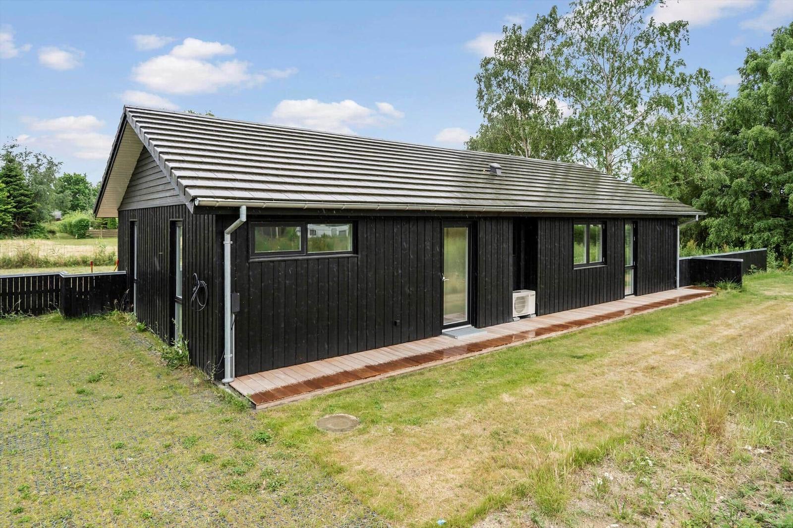 Moderne Holzhütte mit Terrasse und Garten. Schwarze Fassade, große Fenster.