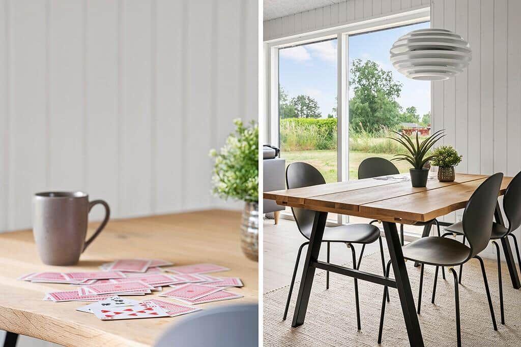 Holztisch mit Stühlen, Pflanzen und Fensterblick auf Grünflächen.